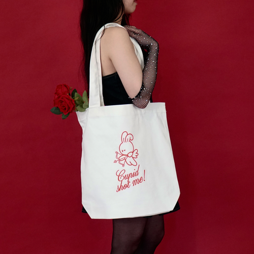 Woman holding a white tote bag with red text and bunny graphics against a red background